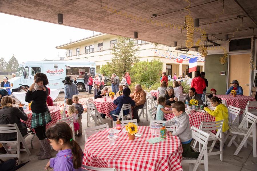 People sitting at outdoor tables with food trucks, crafts, and activities.